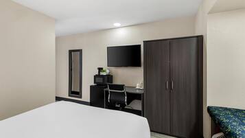Una habitación de hotel con una cama, un escritorio con computadora, televisor y armario.