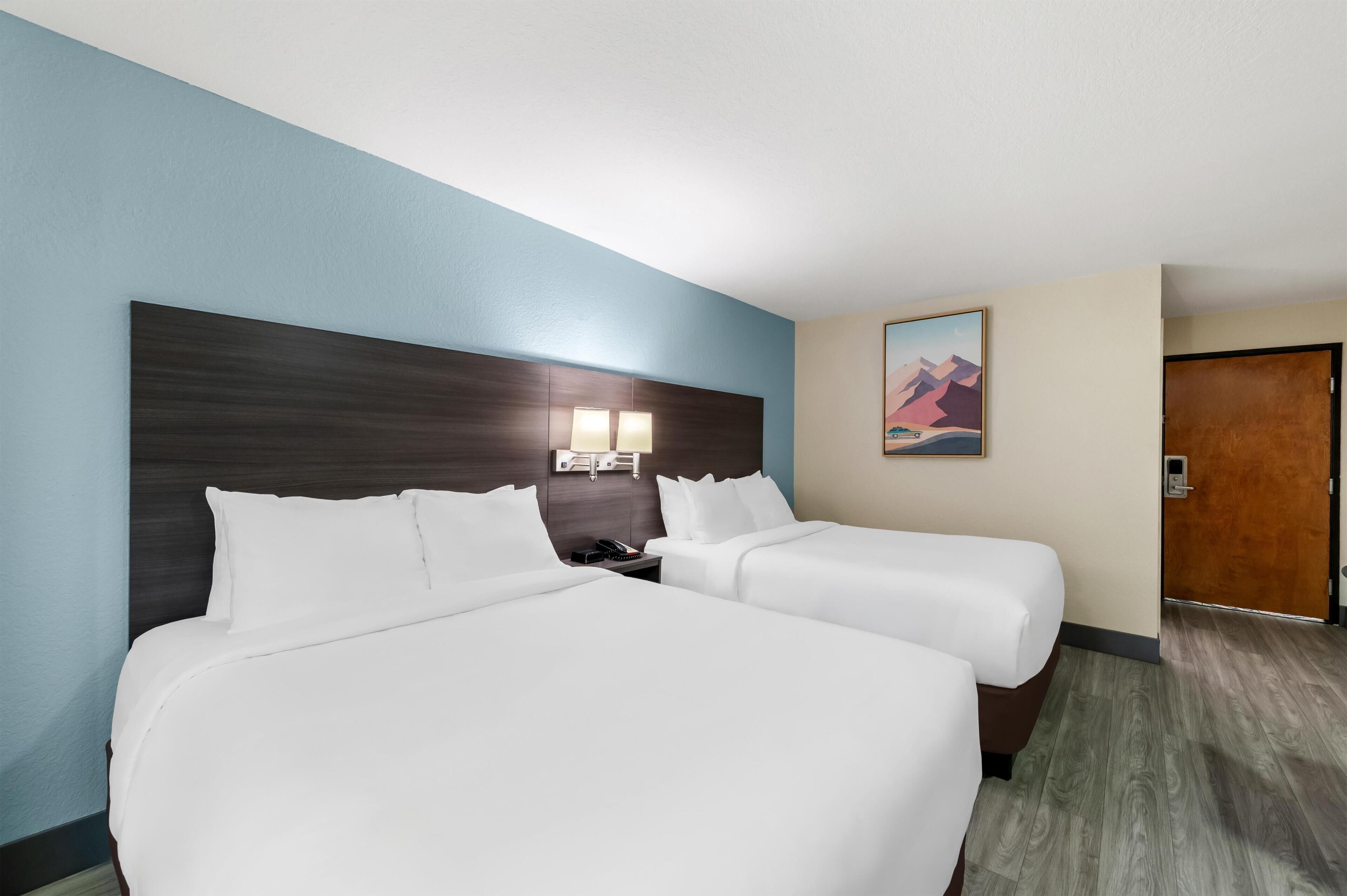 A hotel room with two beds, a nightstand, a lamp, and a painting on the wall.