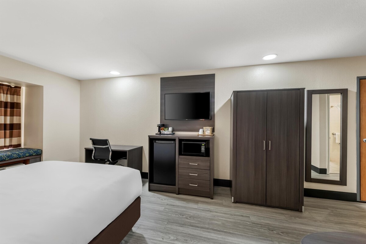 Una habitación de hotel con cama, escritorio, televisor, armario y puerta de baño.