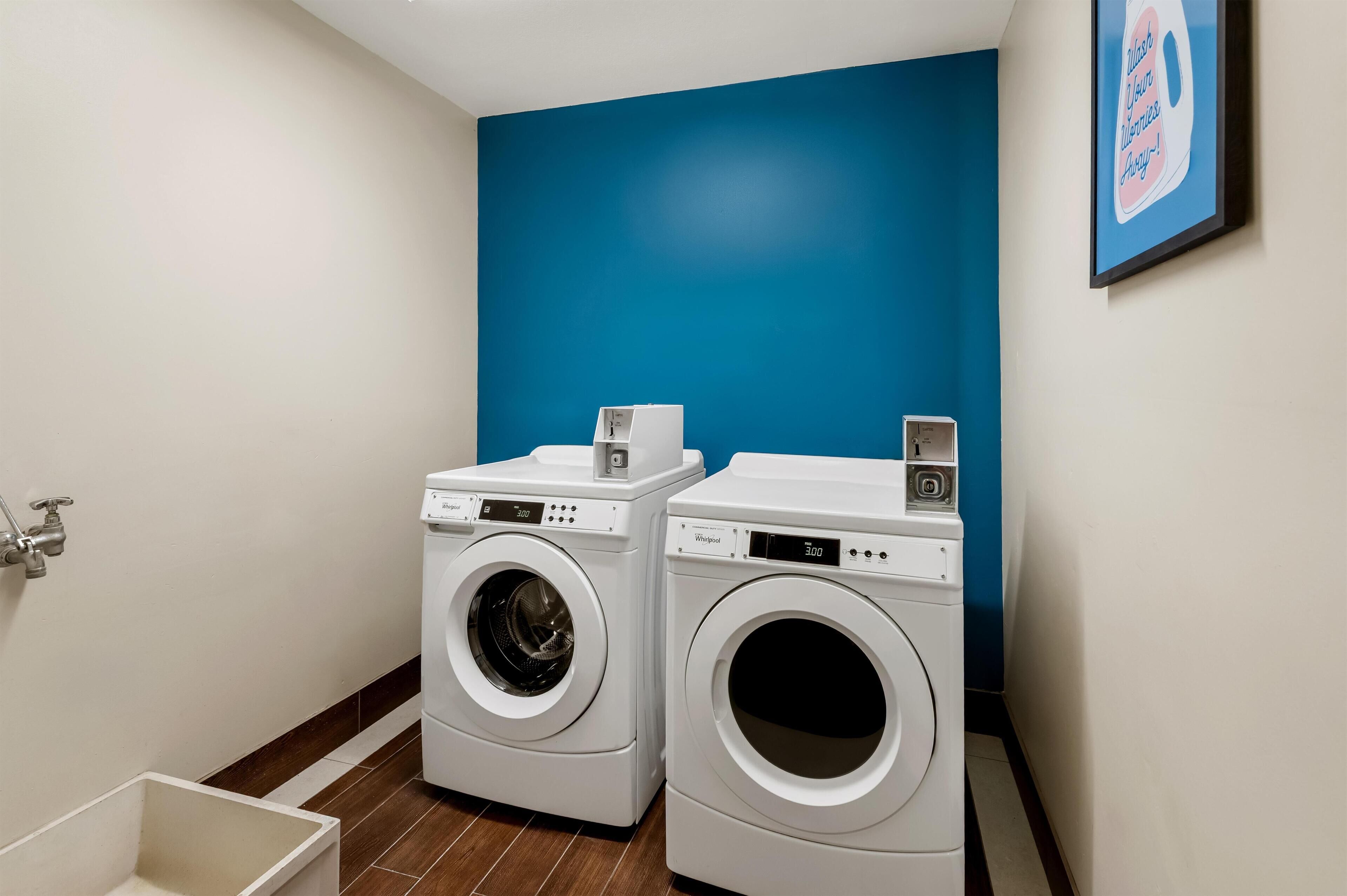 Un cuarto de lavandería con dos lavadoras Whirlpool de carga frontal, un lavamanos pequeño y una pared de acento azul.