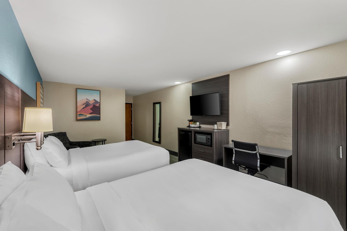 Habitación de hotel con dos camas, un escritorio, un televisor de pantalla plana, una lámpara y un cuadro en la pared.