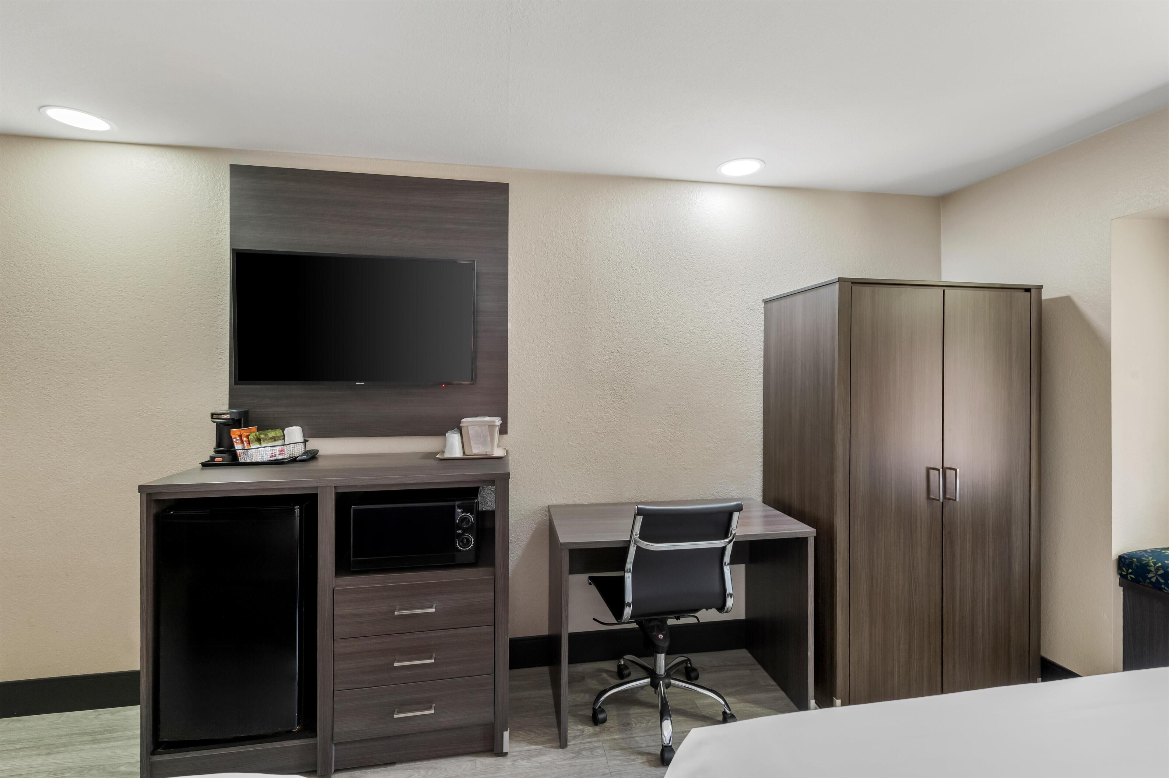 A hotel room with a desk, a chair, a wardrobe, a television, and a coffee maker.
