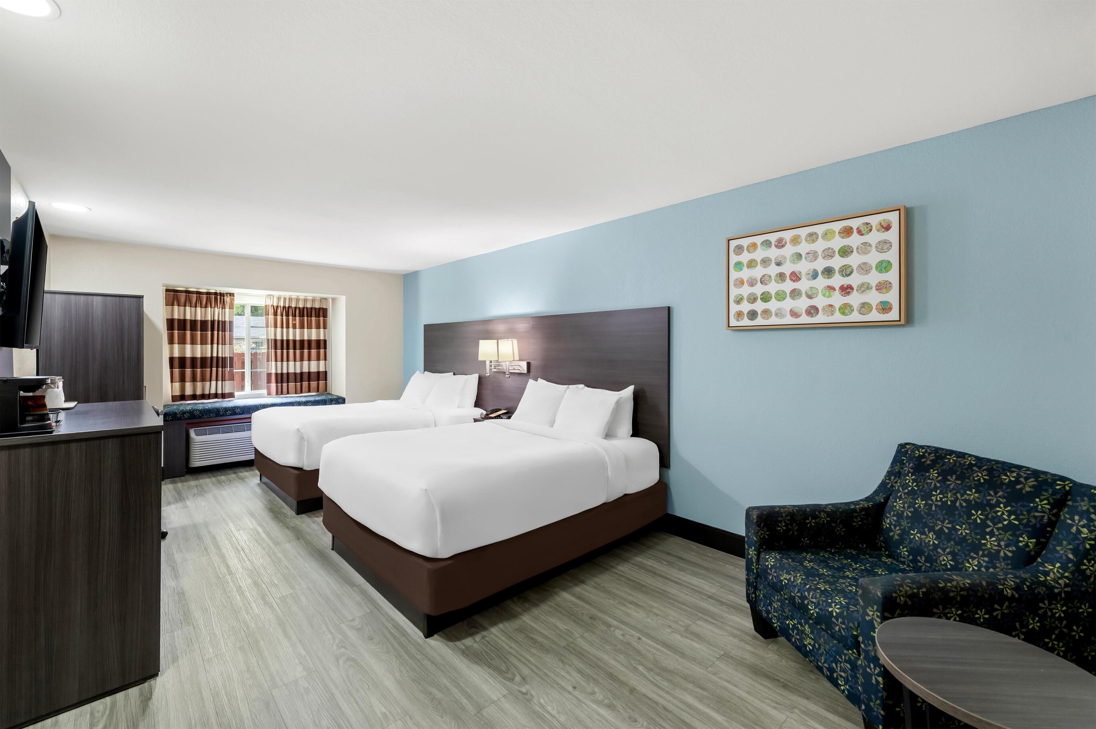 Habitación de hotel con dos camas, un escritorio, una silla y una obra de arte colgada en la pared.