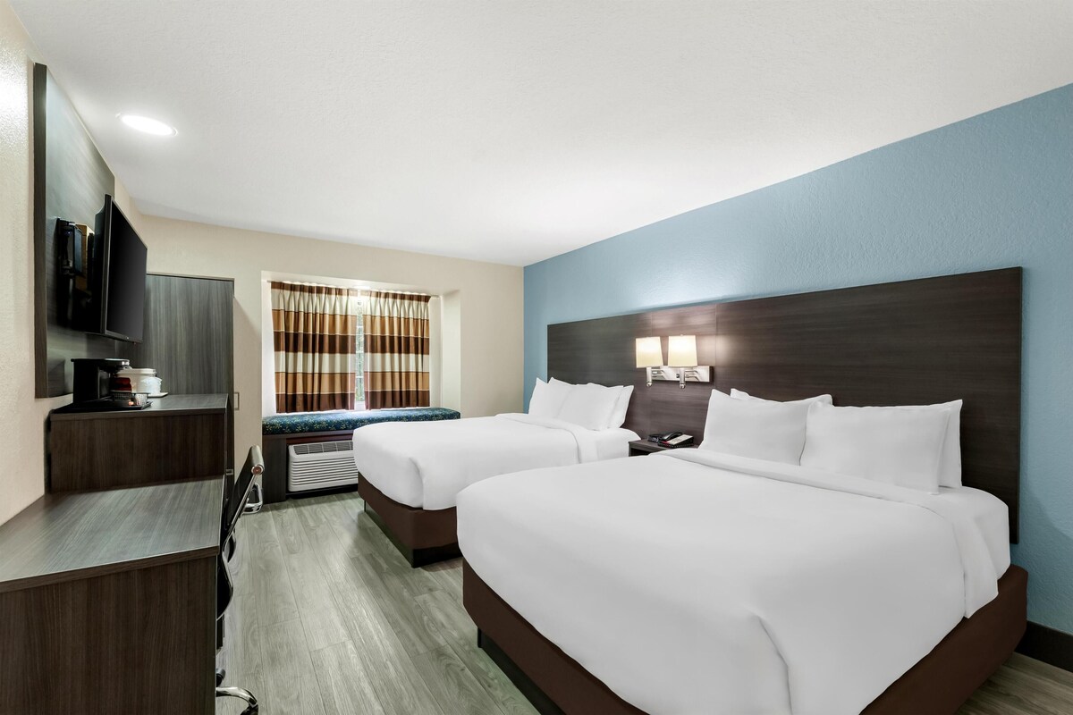 Habitación de hotel con dos camas, televisión, escritorio y ventana con cortinas.