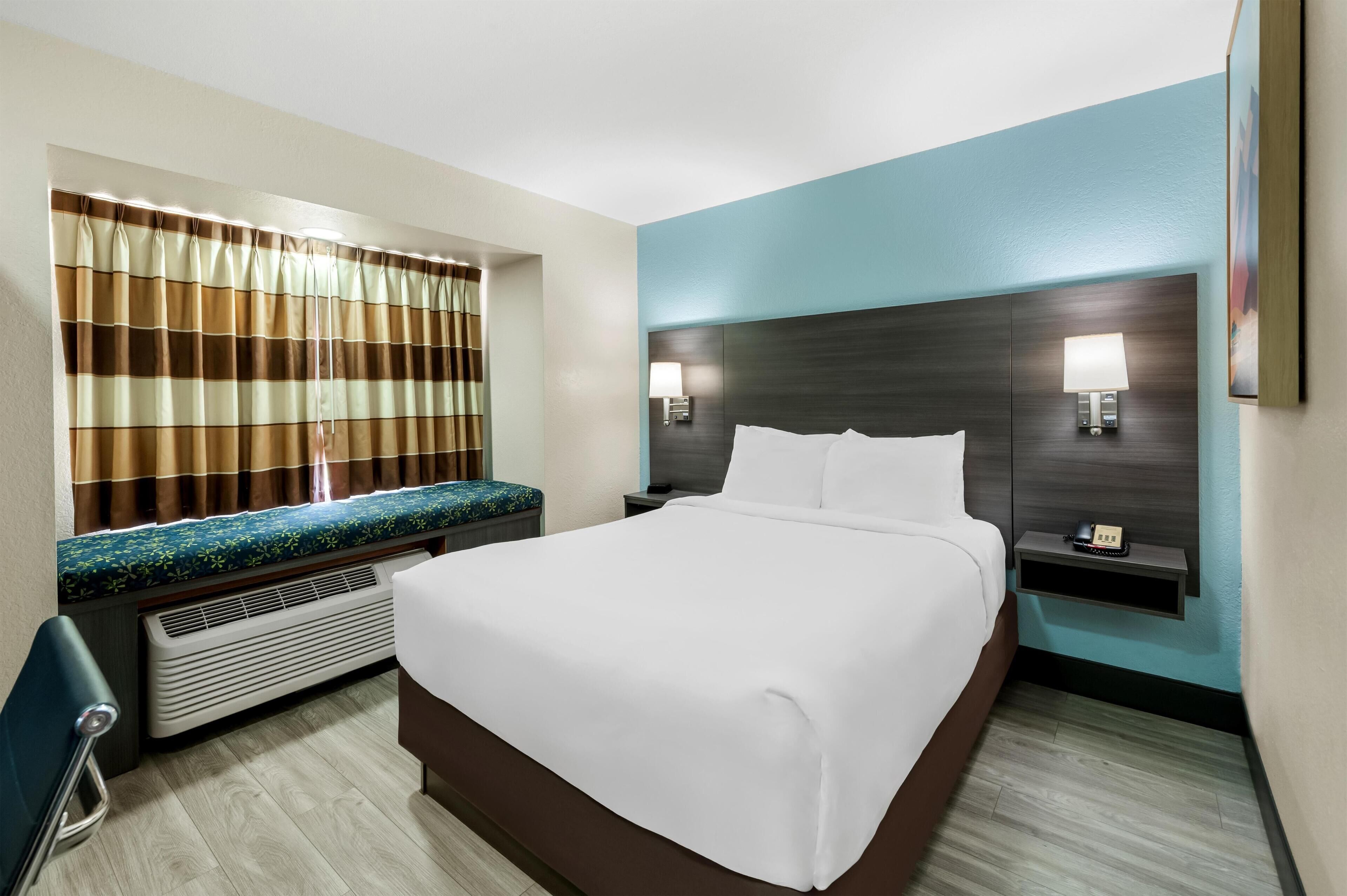 Une chambre d’hôtel dotée d’un grand lit, d’un coin salon avec un banc, d’un téléviseur fixé au mur et d’une table de chevet avec une lampe et un téléphone.