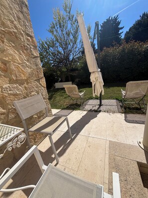 Une terrasse avec des meubles d’extérieur, un mur en pierre et un arbre en arrière-plan.