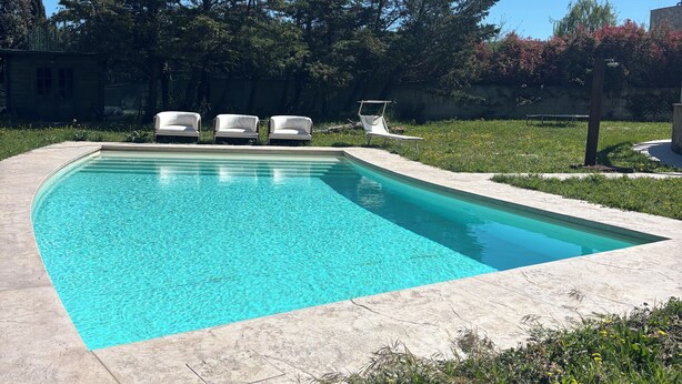 Une piscine rectangulaire à l’eau d’un bleu limpide, entourée d’une terrasse en béton. Trois chaises longues blanches sont alignées le long du bord de la piscine.
