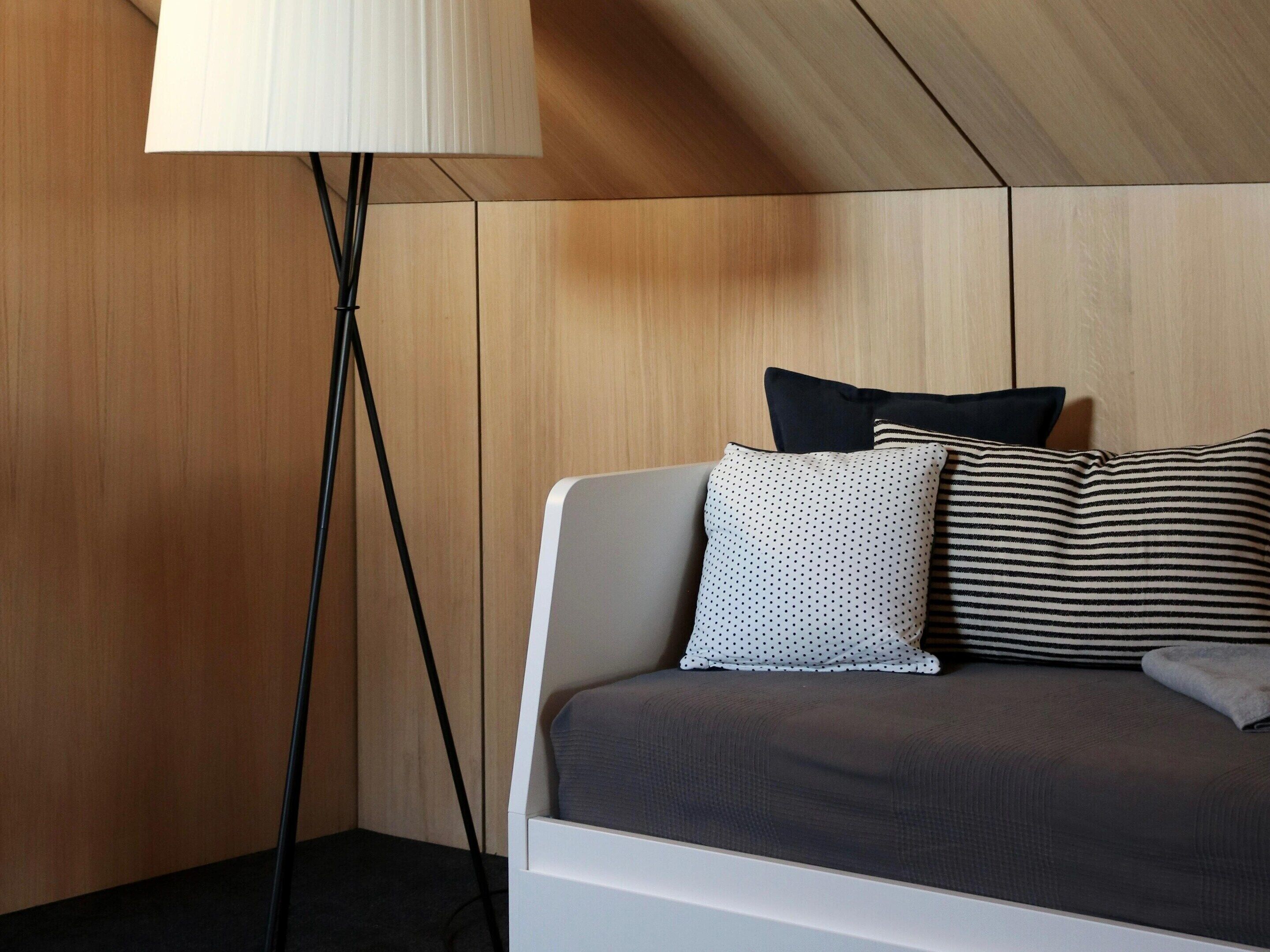A modern room with a bed, a floor lamp, and wooden panel walls.