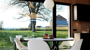 A modern dining area with a table and chairs, a view of a tree and a building outside, and a pendant light above the table. - Modern Design House With Sauna 'arduenna Silva' (La Roche-en-Ardenne)
