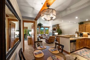 A spacious living area with a large wooden ceiling beam, a chandelier, and a dining table with magazines. - Black Bear 203 (Crested Butte)