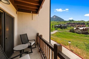 Ein Balkon mit zwei Stühlen und einem Tisch, mit Blick auf eine gebirgige Landschaft und Gebäude.