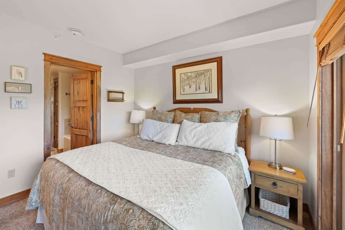 A bedroom with a bed, bedside lamps, a wooden door, and a framed picture on the wall.