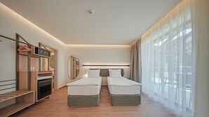 Une chambre d’hôtel moderne avec deux lits simples, un banc en bois, un miroir, un téléviseur intégré et de grandes fenêtres avec des rideaux légers.