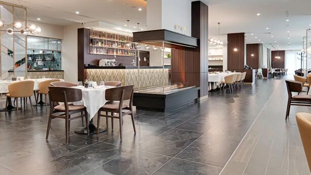 Un intérieur de restaurant moderne avec un bar central, plusieurs tables et un sol carrelé élégant.