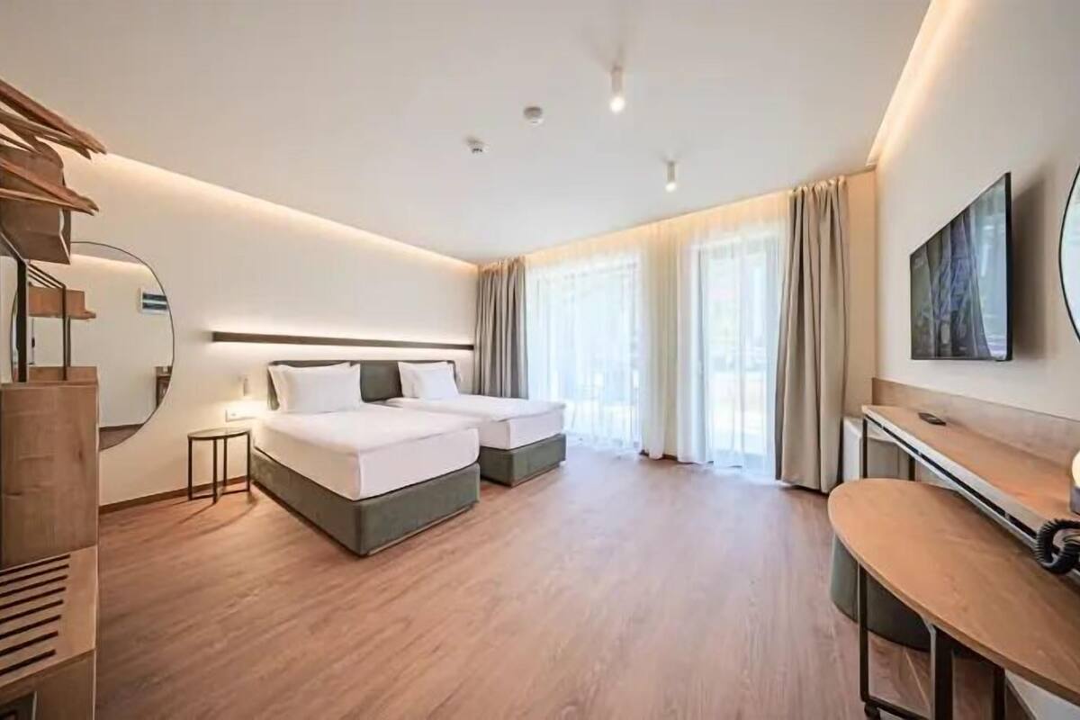 A modern hotel room with a double bed, a desk, a chair, and a large mirror.