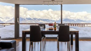 Een eetgedeelte met een tafel voor vier personen, een fles champagne en uitzicht op besneeuwde bergen.