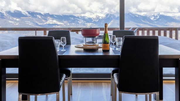 Een eettafel met stoelen, een fles champagne en een rode pot, met uitzicht op bergen.