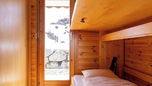 Een houten kamer met een bed, een deur die naar buiten leidt, en een stenen muur die door de deur zichtbaar is.