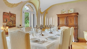 Een eetkamer met een tafel voor zes personen, een kroonluchter en een groot raam.