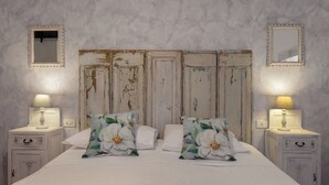 Een slaapkamer met een bed, twee nachtkastjes, twee spiegels aan de muur en een rustiek houten hoofdeinde.