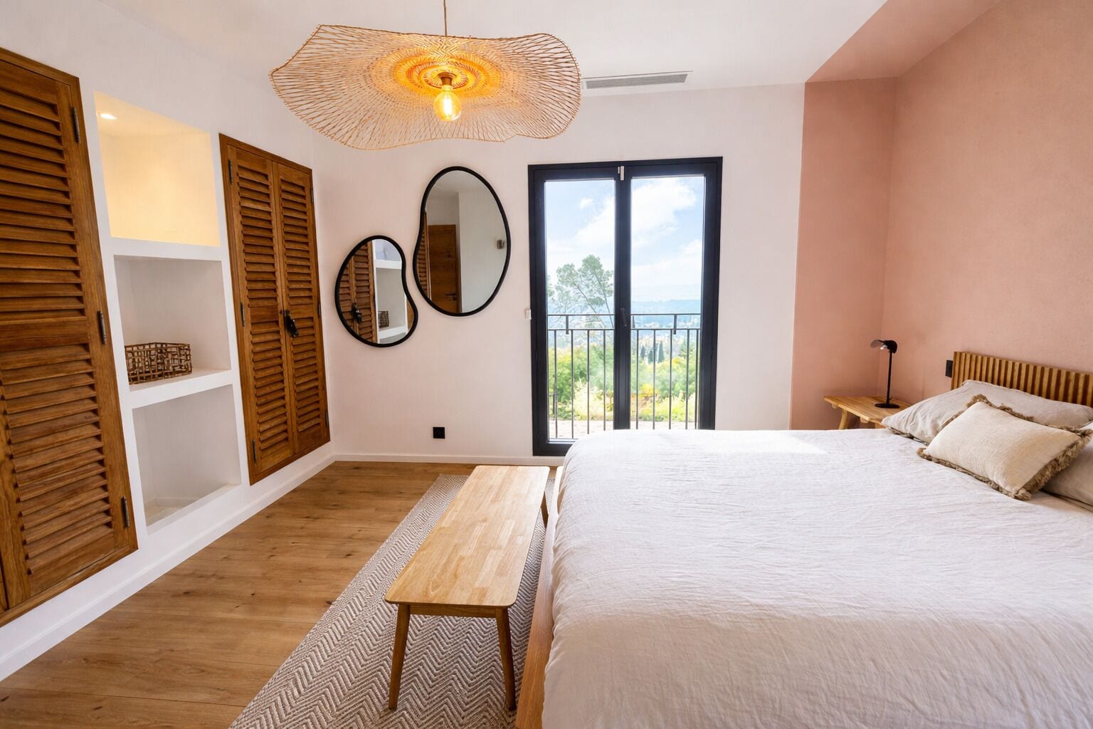 Ein Schlafzimmer mit Bett, einer Holzbank, einer Hängeleuchte, einem Balkon und Blick ins Grüne.