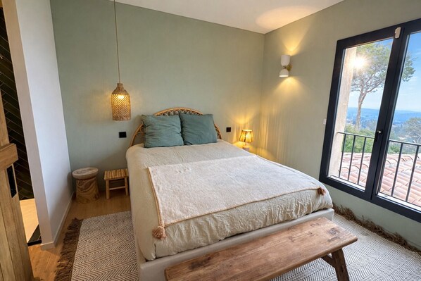 A bedroom with a bed, bedside lamps, a window with a view, and a wooden bench. - Upscale Provencal villa with panoramic views, pool and outdoor bar (Lorgues)