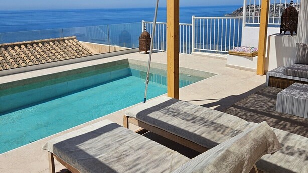 Zona de piscina con sillones de descanso, una pérgola y vistas al mar.