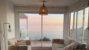 Una sala de estar moderna con dos sofás, una mesa de centro y un gran ventanal con vista al mar.