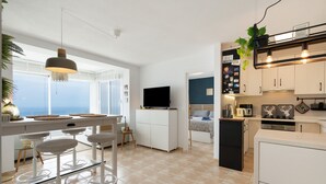 Una cocina moderna con televisor, taburetes de bar y vista al mar.
