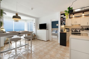 Una cocina moderna con televisor, taburetes de bar y vista al mar.