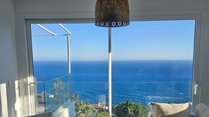 Una sala de estar moderna con un gran ventanal que da a un balcón con vistas al mar.