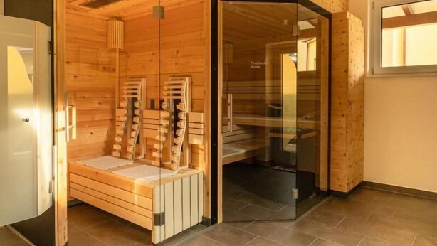 A sauna room with wooden walls and a glass door, a bench, and a towel rack. - Hotel Gut Sein  (Sankt Georgen im Lavanttal)