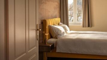 A bedroom with a bed, a nightstand, a vase with flowers, and a window with curtains.