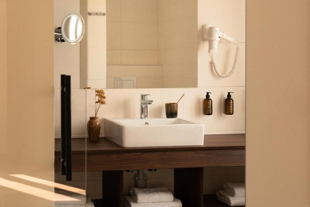 A bathroom with a white sink, a mirror, a hairdryer, and toiletries on the wall.