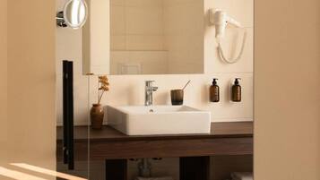 A bathroom with a white sink, a mirror, a hairdryer, and toiletries on the wall.
