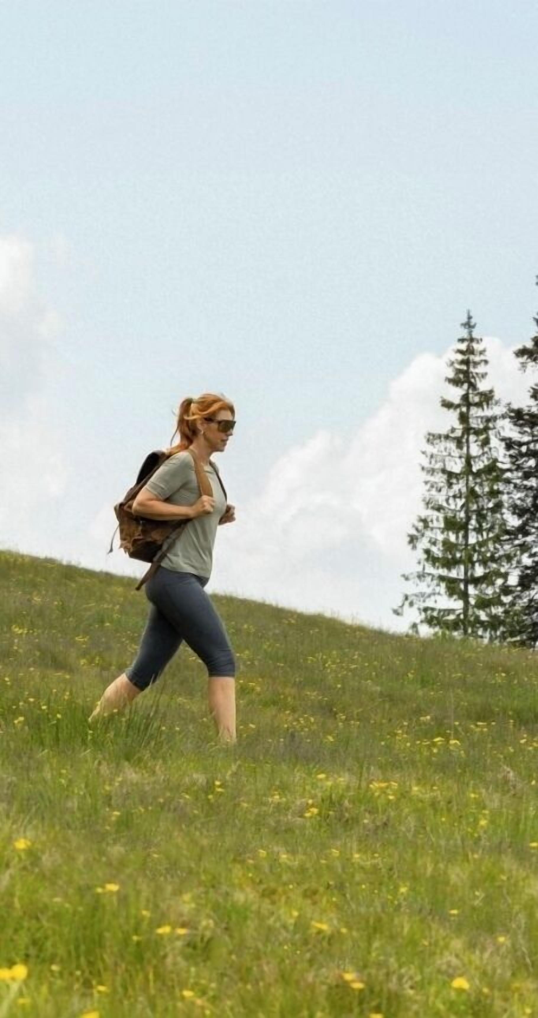 A person walking in a grassy field with a backpack.