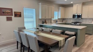 A modern kitchen with white cabinets, a central island, and a dining area with a wooden table and grey chairs. - ✪ Armadillo Rodeo ✪ 1 mile to Baylor, 1/2 mile to Magnolia Silos! (Waco)