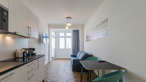 A compact kitchen with a microwave, toaster, and coffee maker, a dining area with a table and chairs, and a sofa in the background. - Nena Apartments Hermannplatz by LESA  (Berlin)
