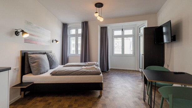 A bedroom with a bed, bedside tables, a desk, a chair, a TV, and a window. - Nena Apartments Hermannplatz by LESA  (Berlin)