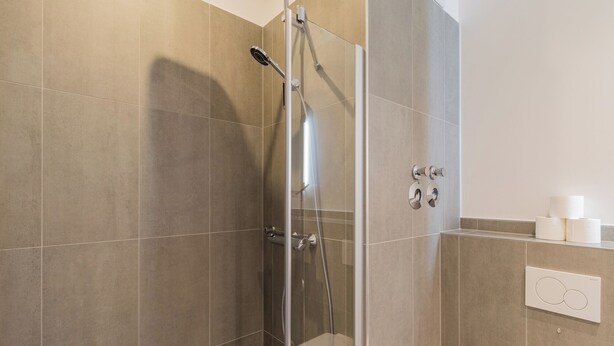 A shower stall with a glass door, a handheld showerhead, and a wall-mounted toilet paper holder. - Nena Apartments Hermannplatz by LESA  (Berlin)