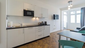 A modern kitchen with white cabinets, a black microwave, and a coffee maker. There is a dining area with a table and chairs, and a TV mounted on the wall. - Nena Apartments Hermannplatz by LESA  (Berlin)