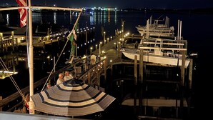 Un port de plaisance de nuit, avec des bateaux amarrés, un drapeau et une personne debout sur un pont.