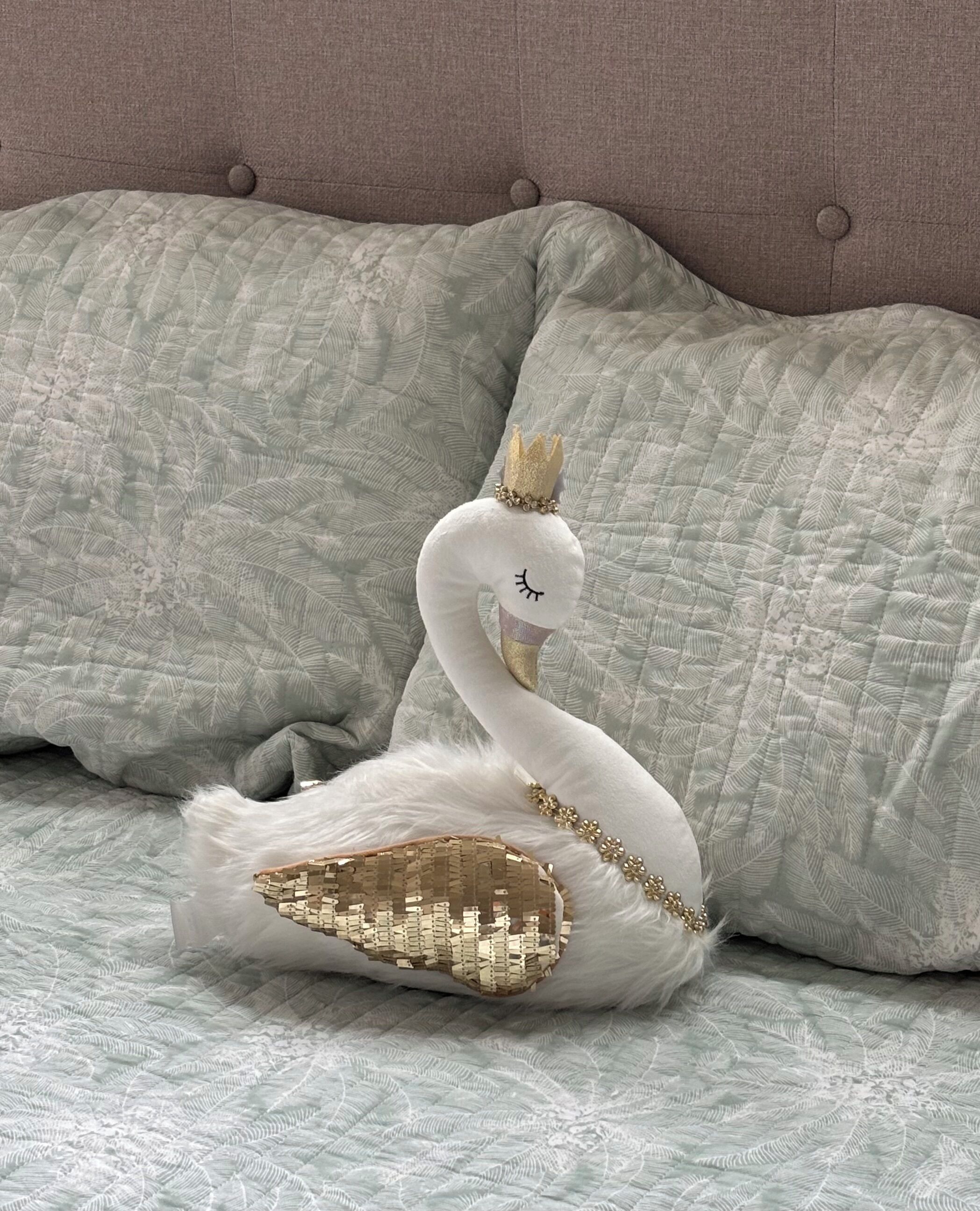 A swan-shaped decorative pillow on a bed with a tufted headboard.
