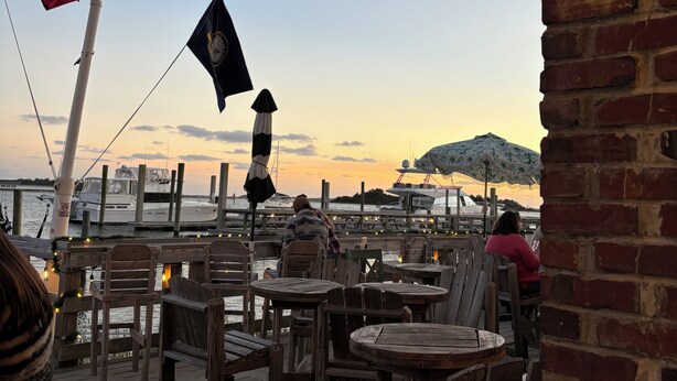 Une terrasse au bord de l’eau, avec des tables et des chaises en bois, des drapeaux et une vue sur l’eau.