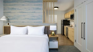 Habitación de hotel con cama, lámpara de noche, mesita de noche, decoración en la pared y kitchenette.