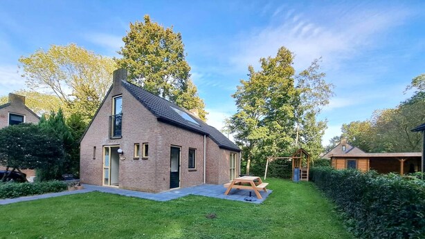 A two-story house with a sloped roof, a small garden, and a wooden play structure. - Elevated Ewijk Cottage for 6 (Ewijk)