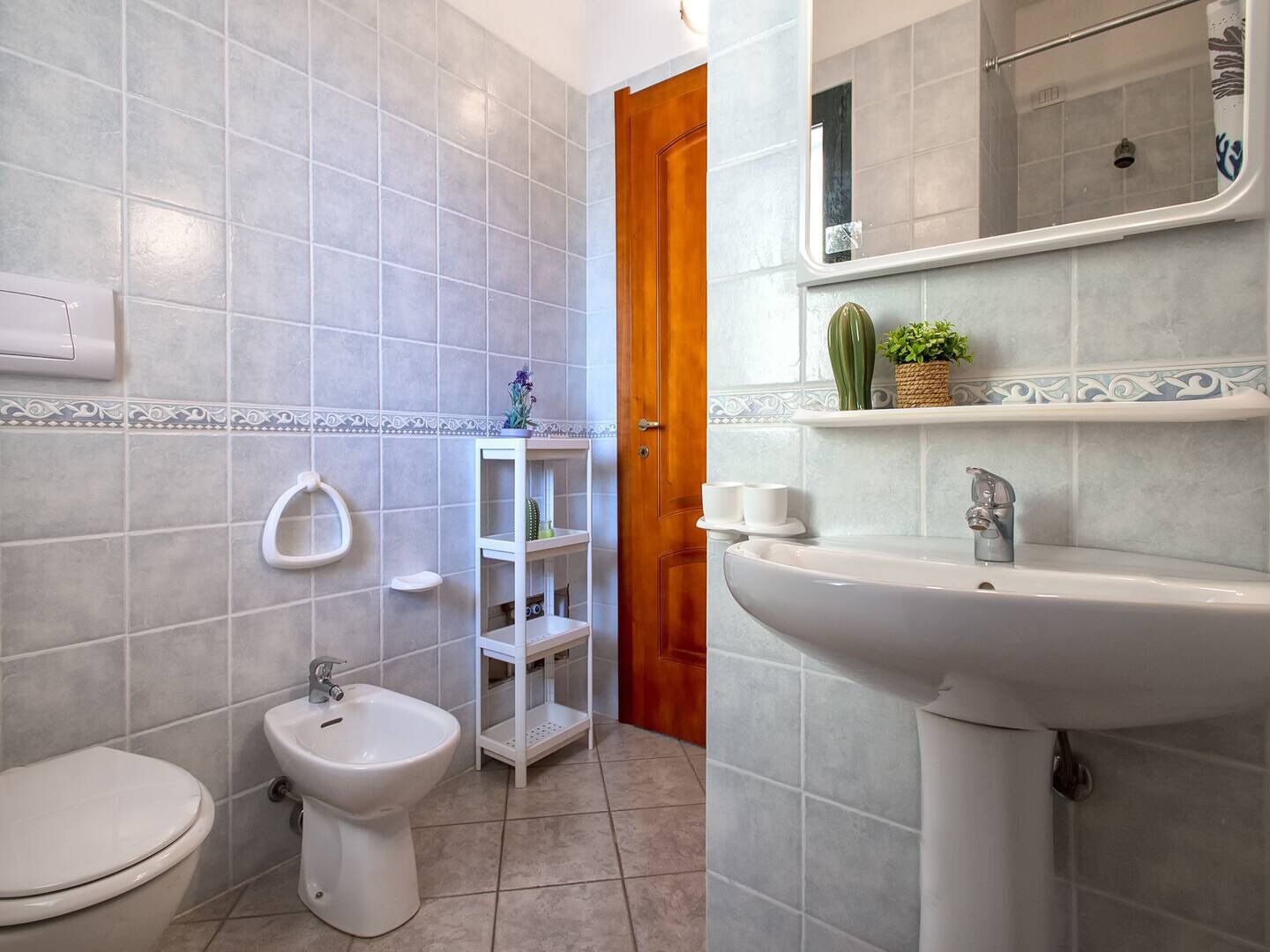 Une salle de bain comprenant des toilettes, un bidet, une étagère avec des articles de toilette et un lavabo.
