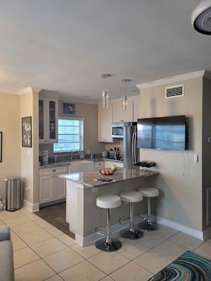 A modern kitchen with a central island, bar stools, a refrigerator, and a television. - 1b1b Resort Condo 2 Blocks to Clearwater Beach (Clearwater Beach)