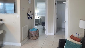 Un salon équipé d’un téléviseur à écran plat, d’une table basse, d’un canapé, d’un tapis à motifs et d’une porte donnant accès à une salle de bain.