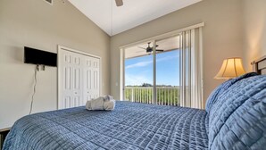 A bedroom with a large bed, a television, a ceiling fan, a window with a view, and a lamp. - Mangrove View 2BR - Pool Hot Tub Gym Access (Ruskin)